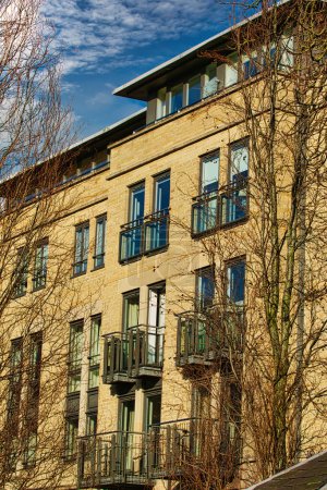 Fassade eines modernen Mehrfamilienhauses mit Balkonen, eingerahmt von blattlosen Bäumen vor blauem Himmel in Harrogate, England.