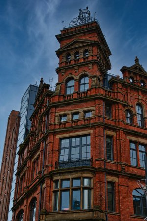 Victorian red brick building with ornate architecture against a dramatic cloudy sky, showcasing a contrast of historical and modern urban design in Leeds, UK.