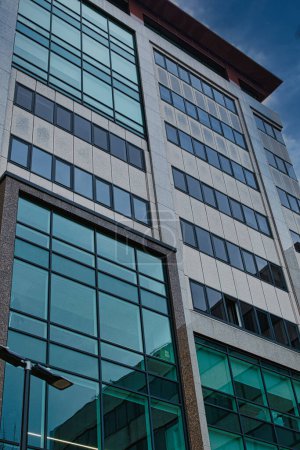Modern office building facade with reflective glass windows against a blue sky in Leeds, UK.
