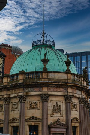 Vintage green dome of a classical building against a blue sky with modern skyscrapers in the background in Leeds, UK.
