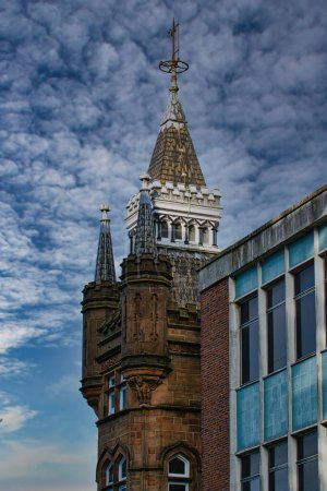 Historischer Turm mit Kirchturm vor dramatischem wolkenverhangenem Himmel und moderner Fassade in Leeds, Großbritannien.