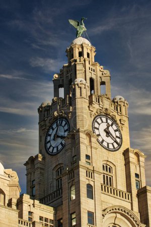 Historischer Uhrenturm vor blauem Himmel mit Wolken, architektonischen Details und einer Statue auf der Spitze in Liverpool, Großbritannien.