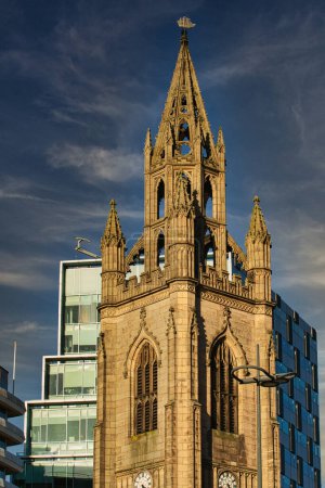 Gotische Kirchturmspitze vor blauem Himmel mit modernen Gebäuden im Hintergrund in Liverpool, Großbritannien.
