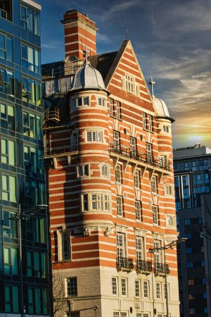 Traditionelles rotes Backsteingebäude neben moderner Glasfassadenarchitektur bei Sonnenuntergang in Liverpool, Großbritannien.