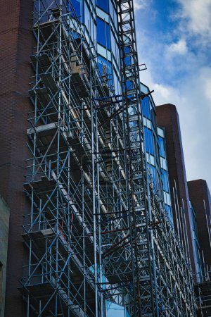 Foto de Estructura de andamios compleja en el lado de un edificio moderno con fachada de vidrio contra un cielo azul en Leeds, Reino Unido. - Imagen libre de derechos