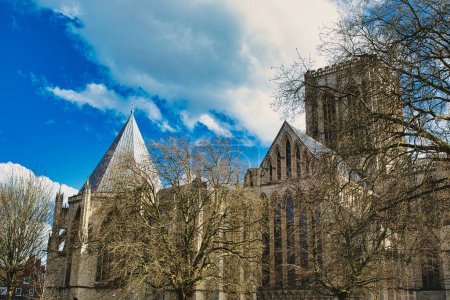 Photo for Historic medieval cathedral with Gothic architecture, featuring pointed arches and robust stone walls, set against a vibrant blue sky with fluffy clouds in York, North Yorkshire, England. - Royalty Free Image