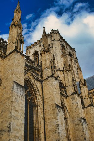 Fachada catedral gótica contra un cielo azul con nubes. La imagen captura la intrincada arquitectura y las imponentes agujas del histórico edificio religioso en York, Yorkshire del Norte, Inglaterra.