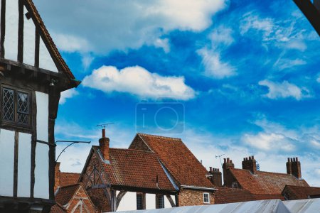 Malerisches europäisches Dorf mit traditionellen Fachwerkhäusern und Terrakottadächern unter einem strahlend blauen Himmel mit flauschigen Wolken in York, North Yorkshire, England.