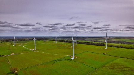 Aerial view of a wind farm with multiple turbines in a lush green landscape under a cloudy sky.