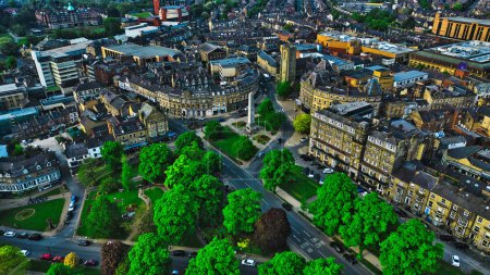 Vista aérea de una ciudad con una mezcla de edificios históricos y modernos, exuberantes árboles verdes y un monumento al obelisco central. Las calles están llenas de coches y la zona parece ser una mezcla de elementos urbanos y naturales.