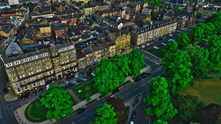 Vue aérienne d'une ville européenne historique avec des rangées de bâtiments anciens, des arbres verts et des rues avec des voitures stationnées. L'architecture présente des bâtiments classiques en pierre avec de grandes fenêtres et des détails complexes.