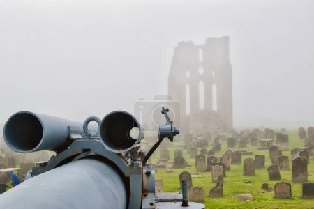A foggy scene of an old cemetery with a large cannon in the foreground and the ruins of a stone building in the background.