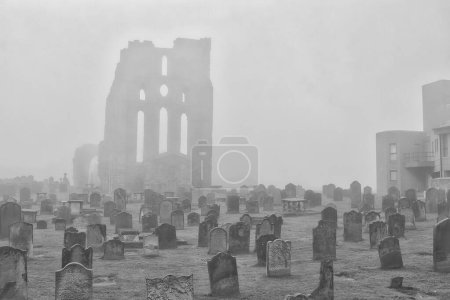 A foggy graveyard with old tombstones and a ruined building in the background.