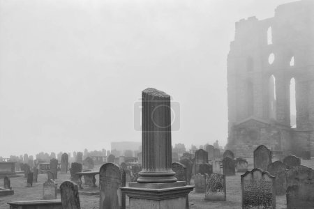 A foggy cemetery with numerous old gravestones and a partially ruined building in the background. The atmosphere is eerie and mysterious.