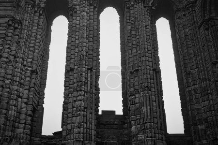 Black and white photo of ancient stone columns with arched openings, part of a historic ruin.