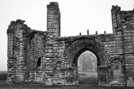 Black and white photo of ancient stone ruins with archways and weathered walls, set against a foggy background.