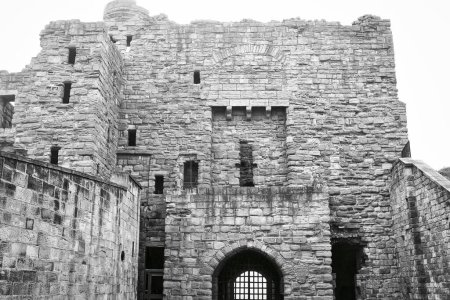 A black and white photo of an old stone castle with a large gate and multiple windows.