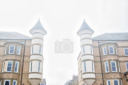 Two symmetrical brick buildings with cylindrical towers and conical roofs on a foggy day.