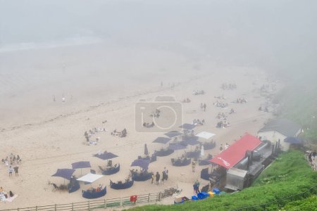 A foggy beach scene with people relaxing under umbrellas and near a food truck.