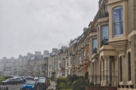 A row of Victorian-style terraced houses on a foggy day, with parked cars along the street.