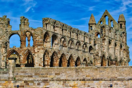 A historic stone abbey ruin with arched windows and intricate architectural details against a blue sky.