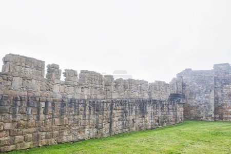 Antike Steinmauer-Ruinen mit grasbewachsenem Vordergrund und nebligem Hintergrund.