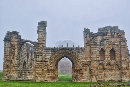 A foggy scene of ancient stone ruins with arched doorways and windows, surrounded by green grass.