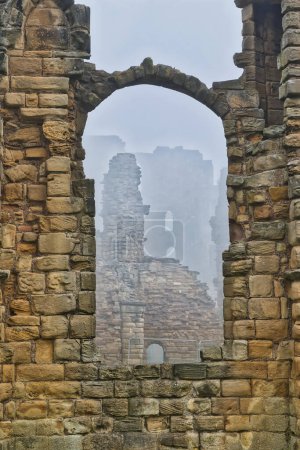 A view through a stone archway of ancient ruins with mist in the background.