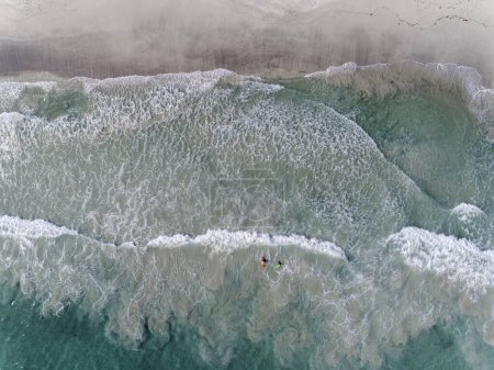 Photo for Aerial drone view of two colourful surfers in the surf at the beach. Clear blue sea water in the summer sunshine. - Royalty Free Image