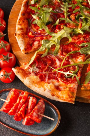 Delicious Italian pizza with prosciutto and arugula on dark background, close up. High quality photo