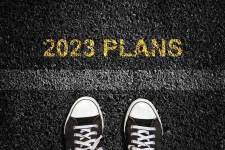 2023. Plans, on an asphalt road surface, and sneakers in front of the lane mark. Top view. The concept of the coming New Year, new plans, and ideas. Business, lifestyle.
