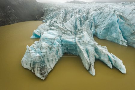 Foto de Vista de arriba hacia abajo de la pared de la lengua de color azul glaciar aéreo y laguna de agua glacial fangosa en Fjallsarlon, Islandia. - Imagen libre de derechos