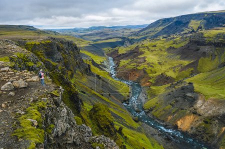 Téléchargez les photos : Vue aérienne au-dessus de la femme avec sac à dos profitant des hauts plateaux glaciaires et de la fosse fluviale près de la cascade d'Haifoss en Islande. - en image libre de droit