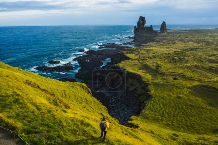 Foto de Caminante hombre de chaqueta amarilla de pie en la cima de la roca en el parque al aire libre en Islandia. Londrangar. - Imagen libre de derechos