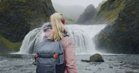 Photo for Iceland, woman with backpack enjoying Stjornarfoss waterfall near Kirkjubaejarklaustur. - Royalty Free Image