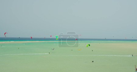 Téléchargez les photos : Grand plan montrant un groupe de kitesurfeurs sur les vagues de l'océan Atlantique à Playa Esmeralda, Fuerteventura, îles Canaries, Espagne. Azur calme vagues de l'océan. Picteresque spectaculaire prise de vue 4k cinématographique - en image libre de droit