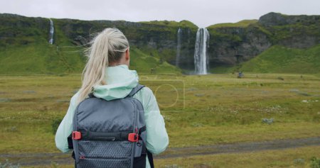 Frau mit Rucksack blickt auf den Wasserfall Seljalandsfoss Island.