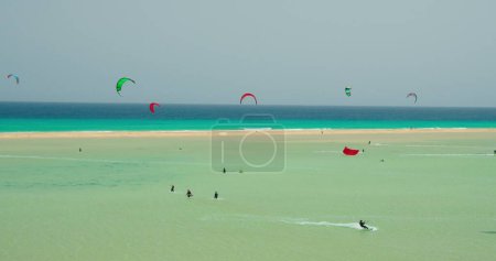 Téléchargez les photos : Grand plan montrant un groupe de kitesurfeurs sur les vagues de l'océan Atlantique à Playa Esmeralda, Fuerteventura, îles Canaries, Espagne. Azur calme vagues de l'océan. Picteresque spectaculaire prise de vue 4k cinématographique - en image libre de droit