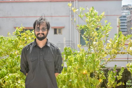 Téléchargez les photos : Un beau jeune homme en noir kabli panjabi debout dans le jardin - en image libre de droit