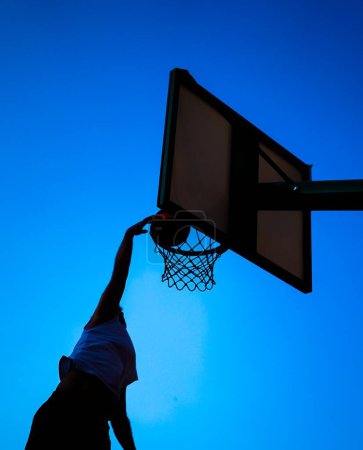Téléchargez les photos : Silhouette d'un homme jouant au basket et plongeant sur le ciel bleu - en image libre de droit