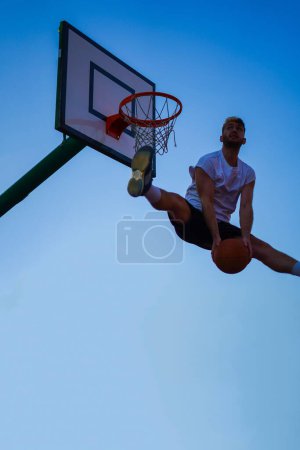 Téléchargez les photos : Homme jouant au basket-ball jmping haut pour faire un dunk inverse sur le ciel bleu - en image libre de droit
