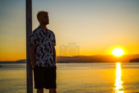 Téléchargez les photos : Jeune homme regardant le coucher du soleil sur la plage - en image libre de droit