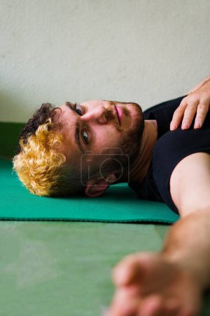 Photo for Blonde man stretching lying at the floor looking at the camera - Royalty Free Image