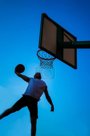 Téléchargez les photos : Homme jouant au basket-ball sauter haut pour dunk sur le ciel bleu - en image libre de droit