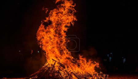 Téléchargez les photos : Feu de joie sur la plage la nuit avec de hautes flammes lors d'une célébration tribale - en image libre de droit