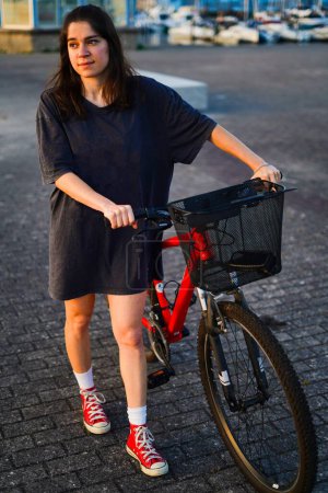 Téléchargez les photos : Jeune fille portant son vélo rouge à travers la promenade - en image libre de droit