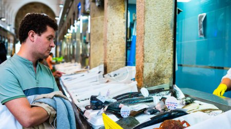 Téléchargez les photos : Jeune homme achetant du poisson dans un marché local - en image libre de droit