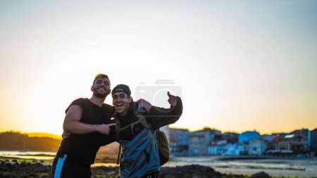 Téléchargez les photos : Amis souriant à la caméra et s'amusant à la plage pendant le coucher du soleil d'été - en image libre de droit