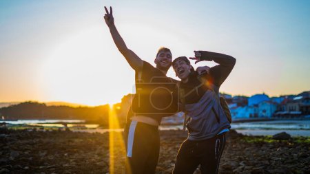 Téléchargez les photos : Amis souriant à la caméra et s'amusant à la plage pendant le coucher du soleil d'été - en image libre de droit