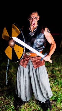 Photo for Angry Viking warrior with black war paint, opening his mouth and holding his sword. - Royalty Free Image
